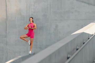 Fototapeta premium Young woman practicing yoga outdoors on a modern structure during daytime