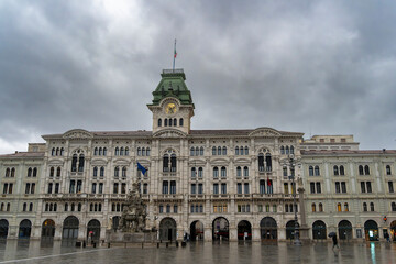 Fototapeta premium Historic European city square with fountain and ornate architecture during rainy weather travel scene. city house Trieste