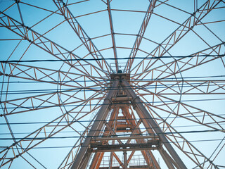 Ferris wheel frame viewed from below. Abstract geometric pattern of metal beams against a clear blue sky. Amusement park architecture structure.