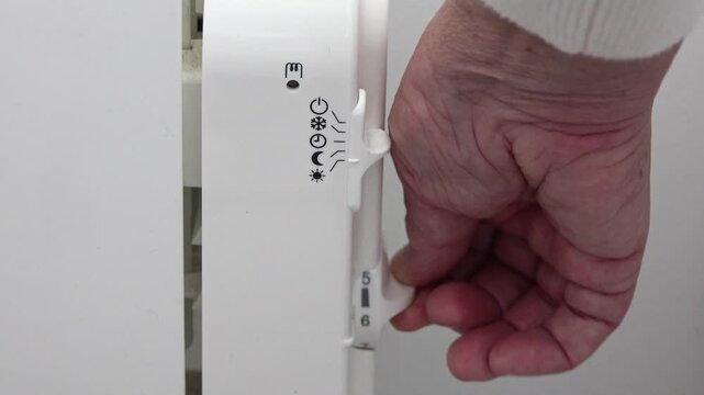 a hand turns on and increases the heating level of a radiator in a room in a house