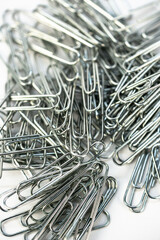 Metal paper clips scattered on a white surface in a random arrangement during daylight hours in an office setting