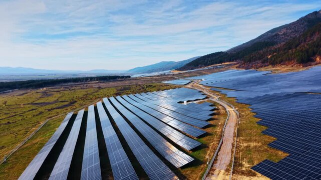 Solar panel field with access road near mountains. View of a large photovoltaic installation showing the perimeter fence and service road in a rural area.