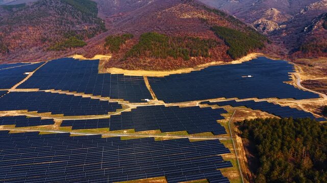 Aerial perspective of solar farm in a mountain valley. High angle view showing the extent of a solar energy facility surrounded by forested hills and mountains.
