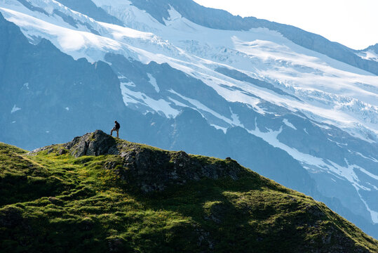 A hiker reached a small mountain summit and viewing towards a muh higer summit