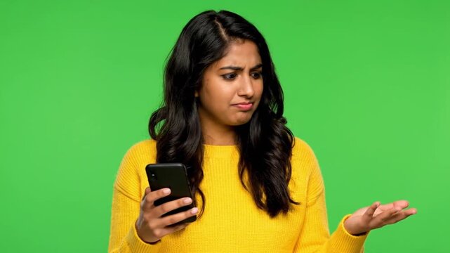 Young woman surprised while using smartphone against green background