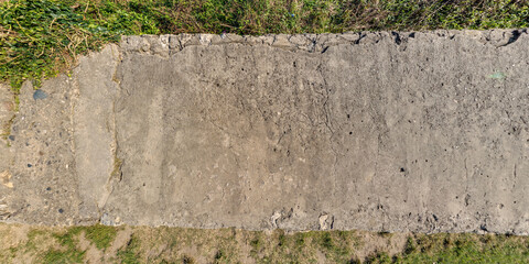top view of textured concrete road with cracks and grass lawn