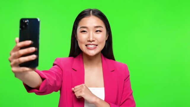 Young Asian businesswoman taking selfie with smartphone on green screen