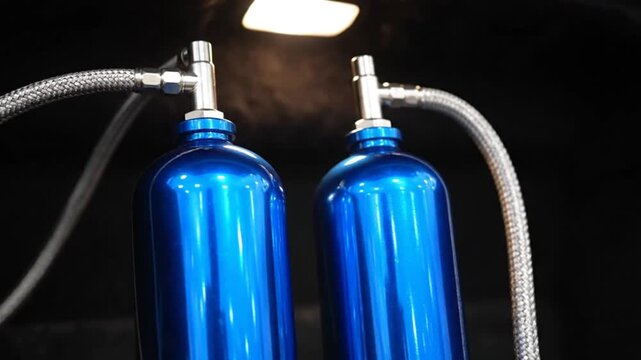 Close-up of two blue nitrous oxide tanks in a car trunk, highlighting automotive performance enhancement.