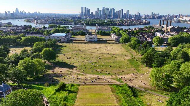 Aerial drone cinematic video over iconic park of Greenwich Royal Observatory, University and Canary Wharf skyscraper complex at the background, London, United Kingdom