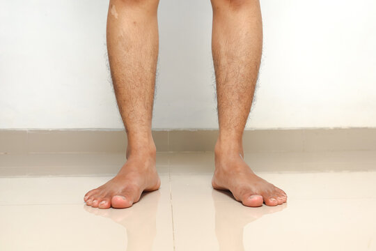 Bare human legs and feet standing on a reflective floor against a white wall