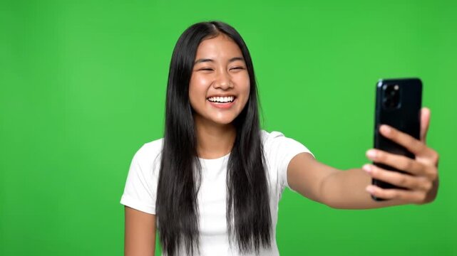 Young Asian woman taking selfie with smartphone against green background