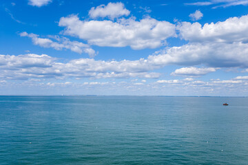 Fototapeta premium A wide view of the calm Atlantic Ocean stretches beneath a sky filled with soft, layered clouds. The tranquil scene features open water, subtle ripples, and a distant boat, evoking a sense of space