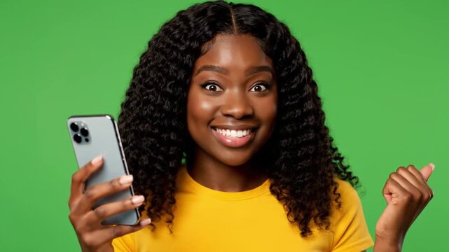 Smiling young woman holding smartphone and giving thumbs up against green background