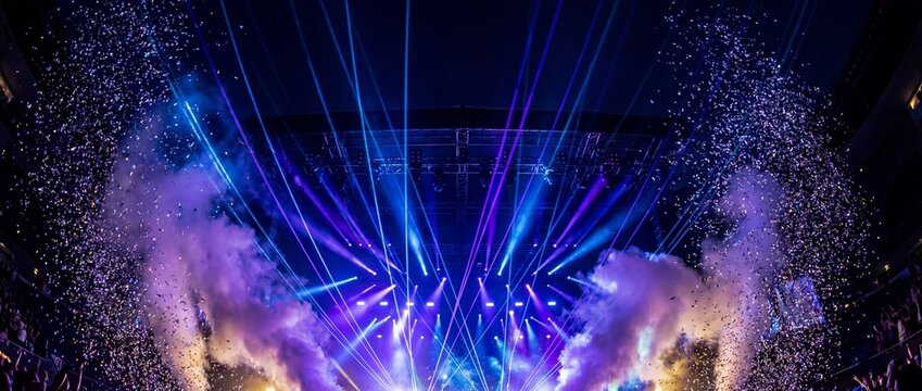 A vibrant concert stage with blue and purple laser lights and pyrotechnics at night