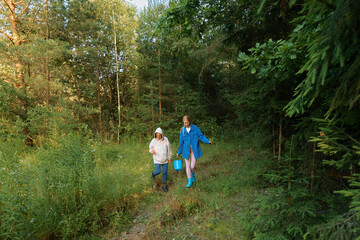 Fototapeta premium Two people walk through a forest path carrying a bucket during a sunny day in the woods