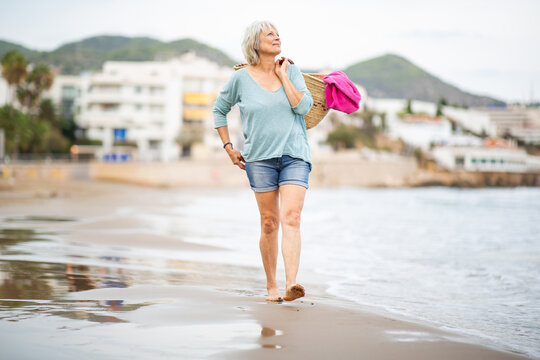 Confident older woman strolling by the sea with beach bag
