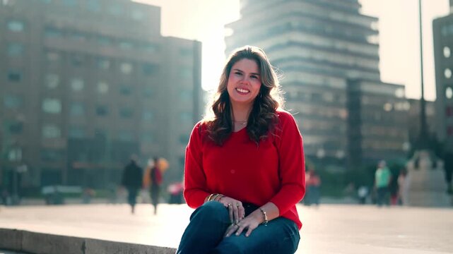 Smiling young Latina walks with calm and confidence under golden morning light near Torre Latinoamericana, just in front of Palacio de Bellas Artes in Mexico City, wearing red top and denim pants