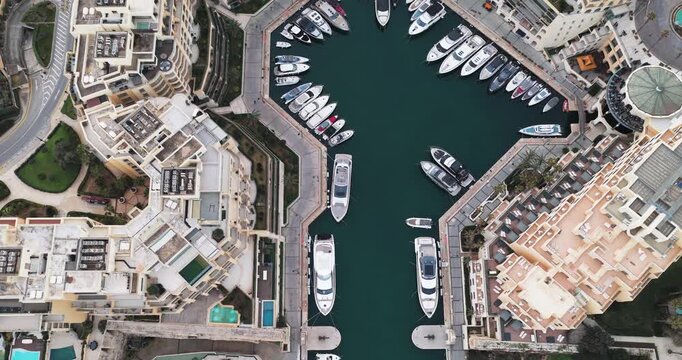Aerial view of the Portomaso Marina where yachts are moored in the dark blue sea, surrounded by buildings, St. Julian, Malta.