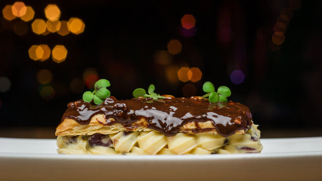 A chocolate &eacute;clair style dessert with cream and cress on a plate in a restaurant at night