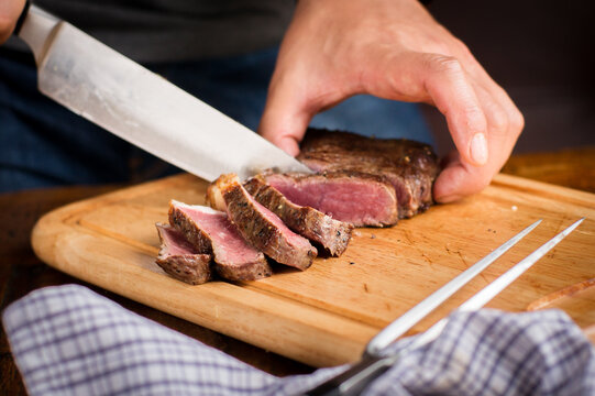 A freshly cooked steak being sliced with a large knife on a wooden cutting board.