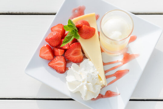 Cheesecake with strawberries and cream and a small cocktail with ice
