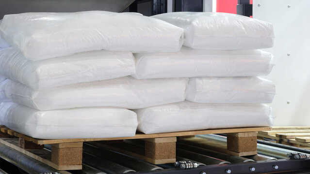 White plastic bags lie on a wooden pallet on a roller conveyor at a distribution warehouse for packaging and delivery
