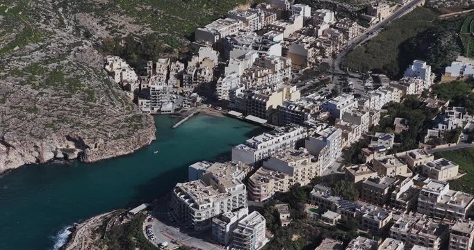 Aerial view of Xlendi Bay's buildings and coastline, the turquoise waters contrasting with the tan buildings, Xlendi, Munxar, Malta.