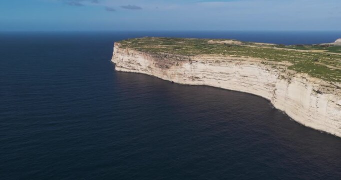 Aerial view of rugged cliffs meeting the deep blue sea, where the island's edge is a stark contrast of white stone and green vegetation, Xlendi, Munxar, Malta.