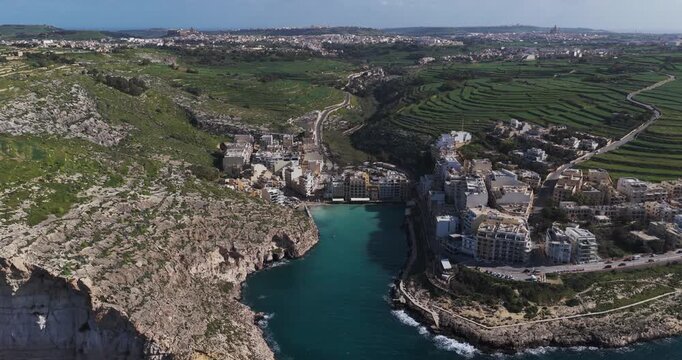 Aerial view of Xlendi Bay, a coastal inlet with turquoise waters nestled between rugged cliffs and buildings, Xlendi, Munxar, Malta.