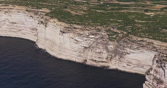 Aerial view of imposing cliffs meet the tranquil sea, showcasing nature's beauty, where the land's edge dramatically embraces the vast waters, Xlendi, Munxar, Malta.