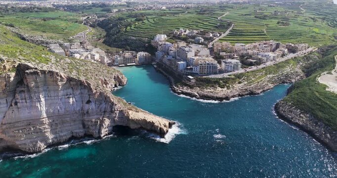Aerial view of Xlendi Bay, where white buildings nestle between the turquoise waters and craggy cliffs, creating a striking contrast, Xlendi, Munxar, Malta.