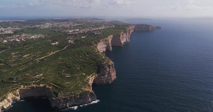 Aerial view of dramatic cliffs meeting the deep blue sea, with lush green terraces contrasting against the rugged coastline, Xlendi, Munxar, Malta.