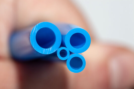 Hand holding several blue polyurethane pneumatic hoses of different diameters for industrial air supply systems and automation fluid transfer isolated on white background for engineering.