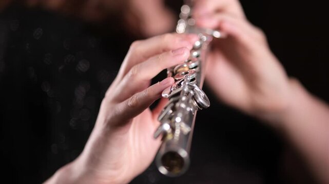 Woman musician playing the flute, hands focused on keys of musical instrument. Classical sound production, performance art.