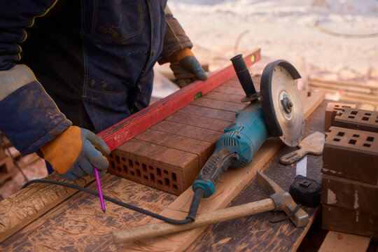 Construction worker grinding brick in snow. Worker shaping brick with grinder on snow-covered site. Mason using power tool to cut brick amid snowy construction environment