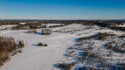 Aerial view of a snow-covered landscape with rolling hills, scattered trees, and clear blue sky in a winter setting, showcasing the beauty of nature