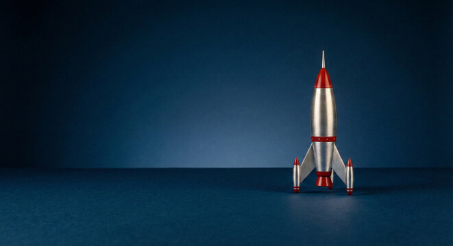 Retro silver rocket ship model ready for launch on dark blue background