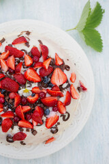 Homemade berry cake with white cream glaze on light wooden background