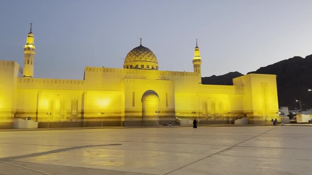 A serene evening shot of the illuminated Sayyid Al-Shuhada Mosque (Uhud Martyrs Mosque) in Medina, Saudi Arabia, standing majestically at the foot of the historic Mount Uhud.