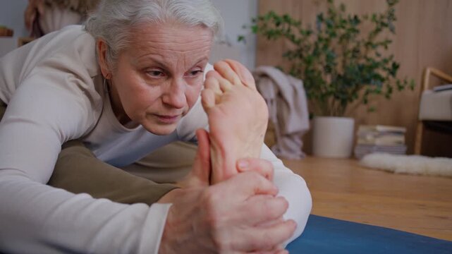 Senior woman grips bare foot in seated stretch with calm focus