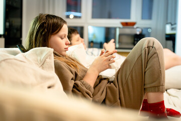 Two children, a boy and a girl, siblings on a sofa at home, deeply focused on a smartphone playing games. Concept of phone addiction, digital dependency