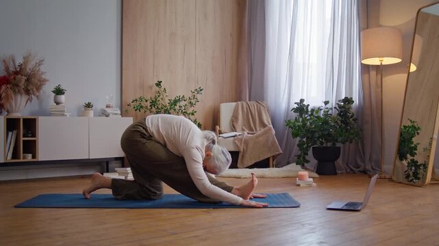 Elderly woman performs kneeling yoga stretch routine at home