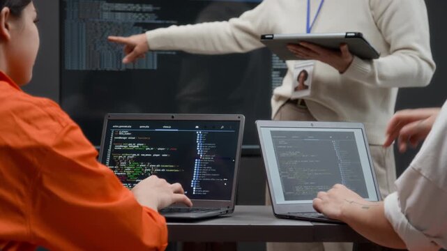 Back view close up shot of two unrecognizable women using laptops with code lines on screen during computer programming class in prison education program, focus on hands typing