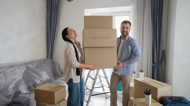 Happy couple holding a stack of cardboard boxes in a new home
