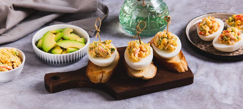 Deviled eggs with tomatoes and avocado on toast on a board web banner