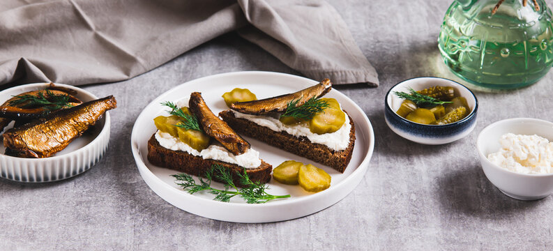 Sandwiches with ricotta, pickles and sprats on rye bread on a plate on a table web banner