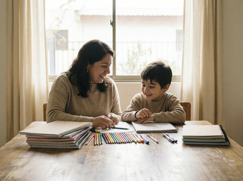 Adulto y ni&ntilde;o preparando cuadernos y &uacute;tiles escolares en mesa iluminada con luz natural frontal suave