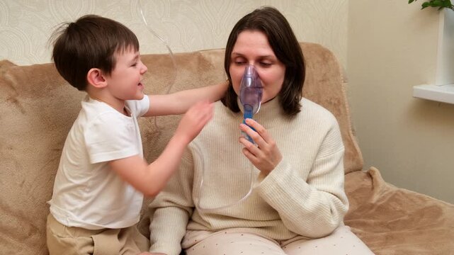 Woman using nebulizer for inhalation treatment while little boy touches her head. Home care for respiratory illness and lung disease.