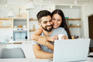 Portrait of a young happy smiling couple using laptop together at home. Wireless technology...
