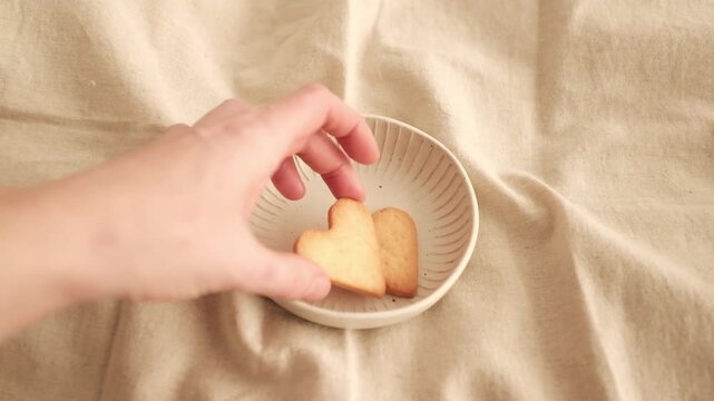 Close-up of heart-shaped butter cookies in a white ceramic bowl. Baked treats on a bright and warm minimalist background. Perfect for romantic holiday baking or Mother&rsquo;s Day, Valentine's Day.